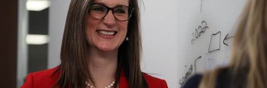 Melissa Albrecht in red jacket and white shirt smiles while talking to colleague. 